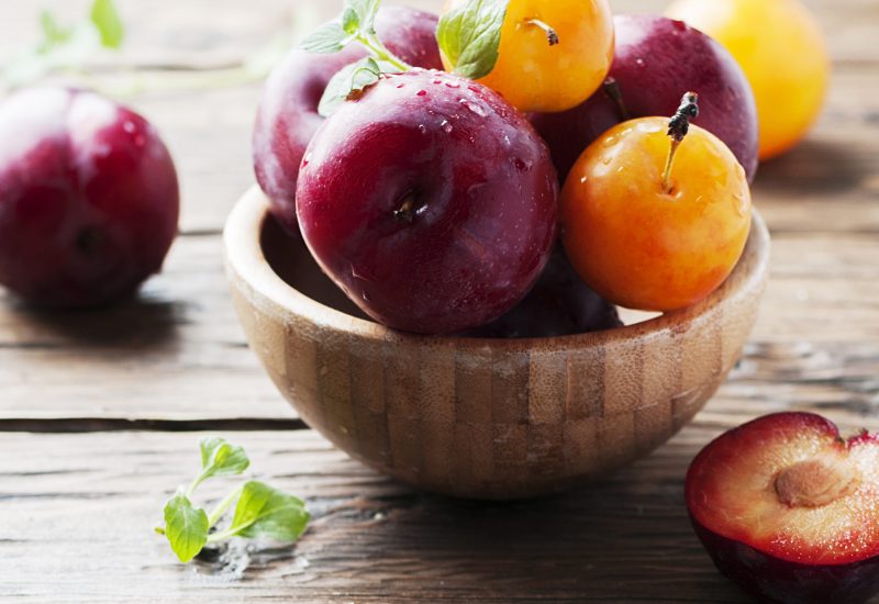Sweet fresh black and yellow plums on the table, selective focus and square image